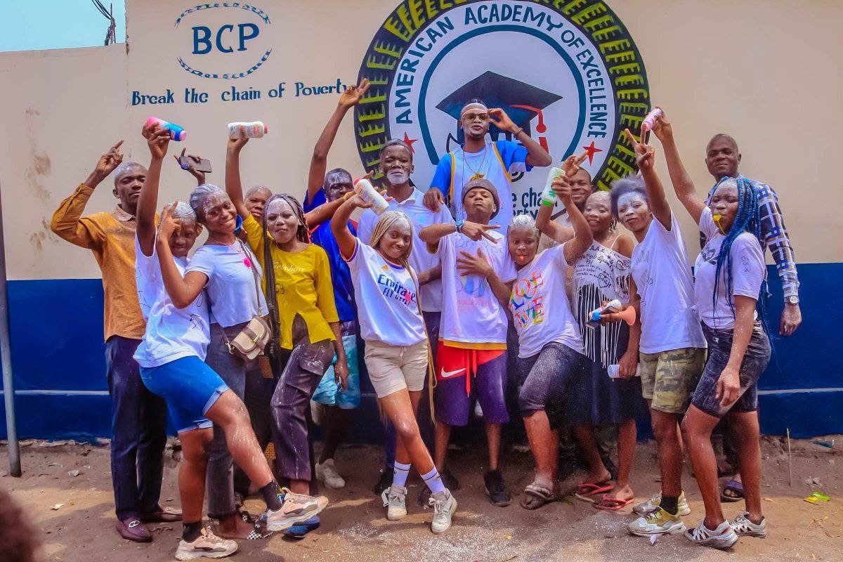 Group celebrating in front of a school wall with the BCP and AAE logos